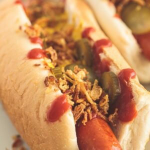 Classic hot dog with mustard, ketchup, pickles and fried onions, white background.