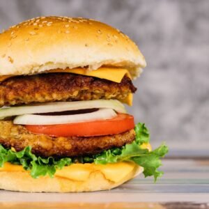 Double juicy burger with vegetables on white table.