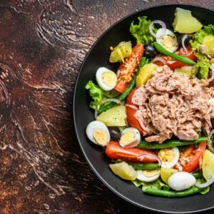 Healthy hearty salad with tuna, green beans, tomatoes, eggs, potatoes and black olives in a plate.