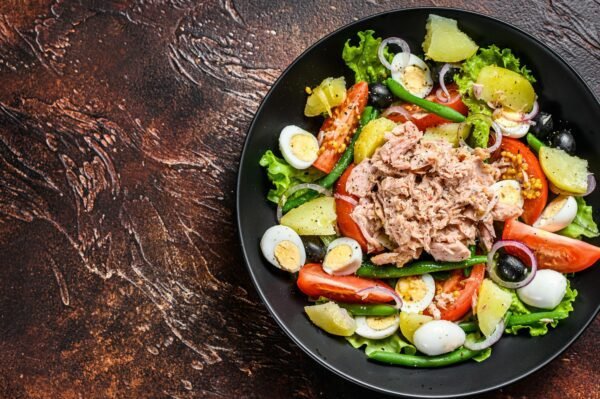 Healthy hearty salad with tuna, green beans, tomatoes, eggs, potatoes and black olives in a plate.